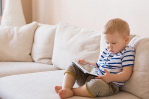 Improve your posture Young child sitting on a sofa with forward neck posture, reading a tablet screen.